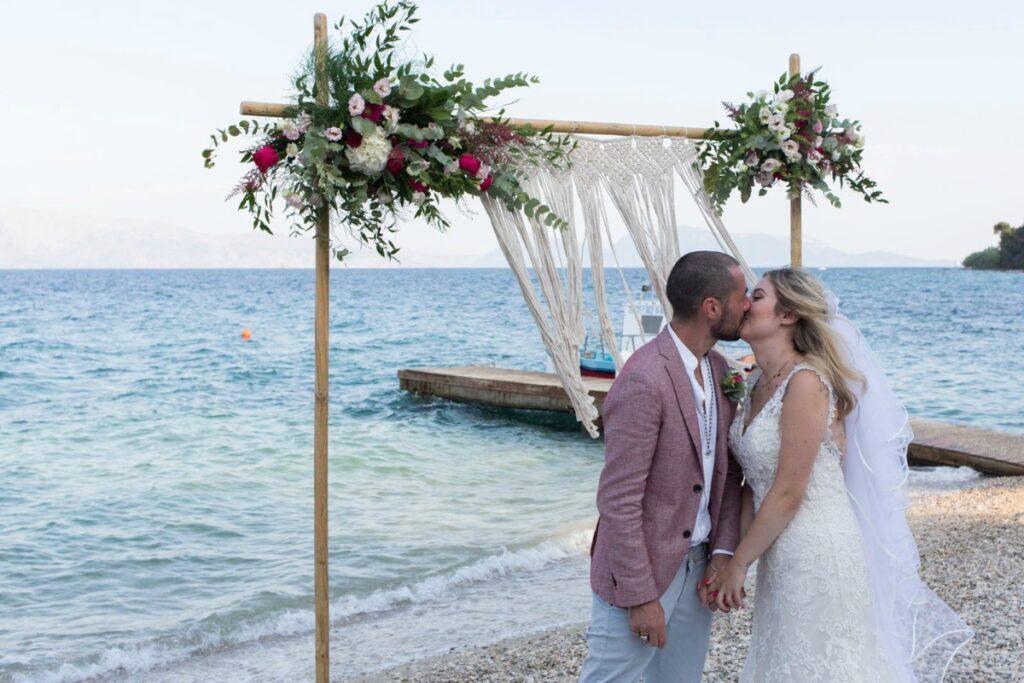 bridal couple embracing in front of flower arch with hanging macrame