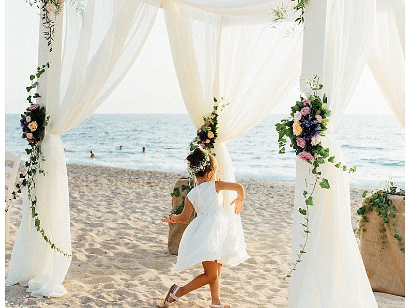 wedding gazebo on beach with white fabric and pink and purple flowers. Girl dancing in the middle