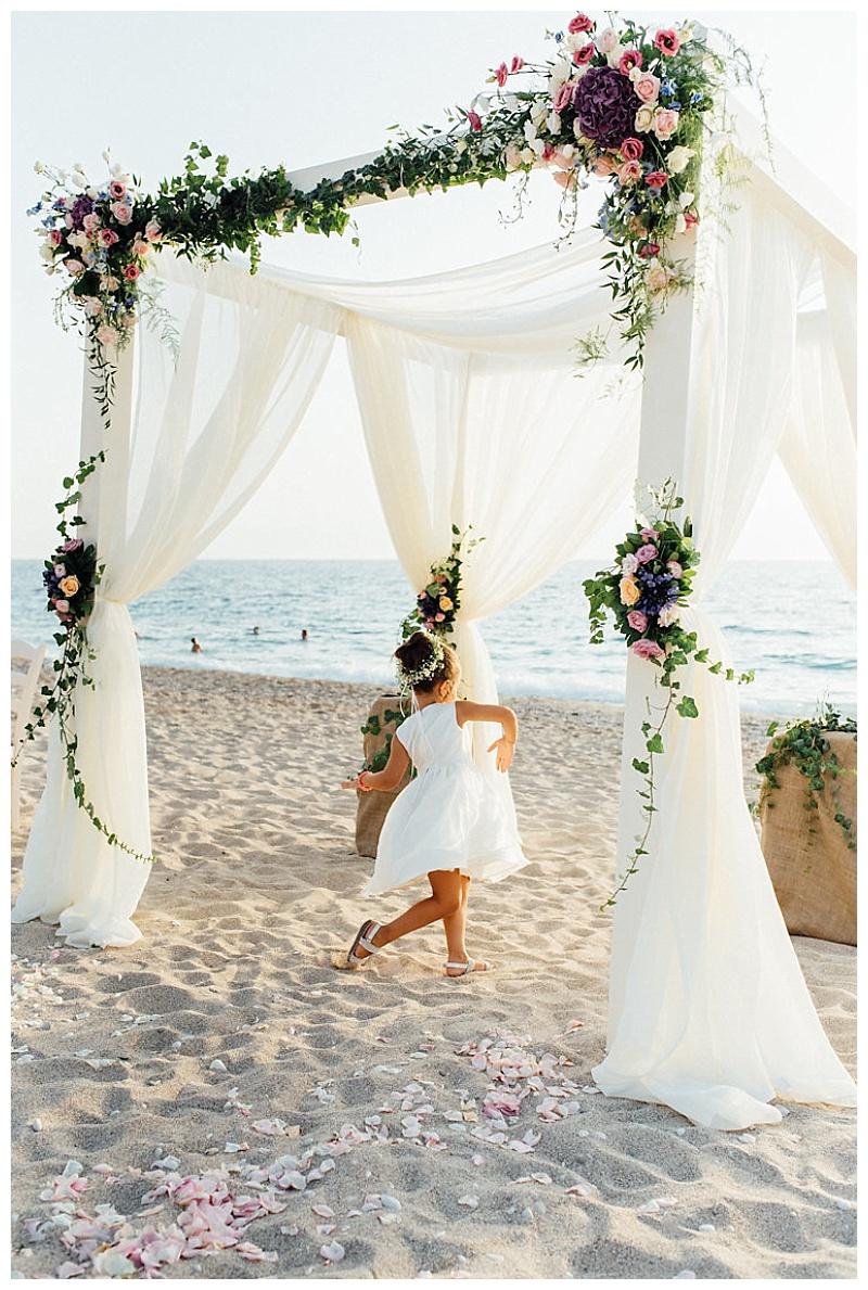 wedding gazebo on beach with white fabric and pink and purple flowers. Girl dancing in the middle